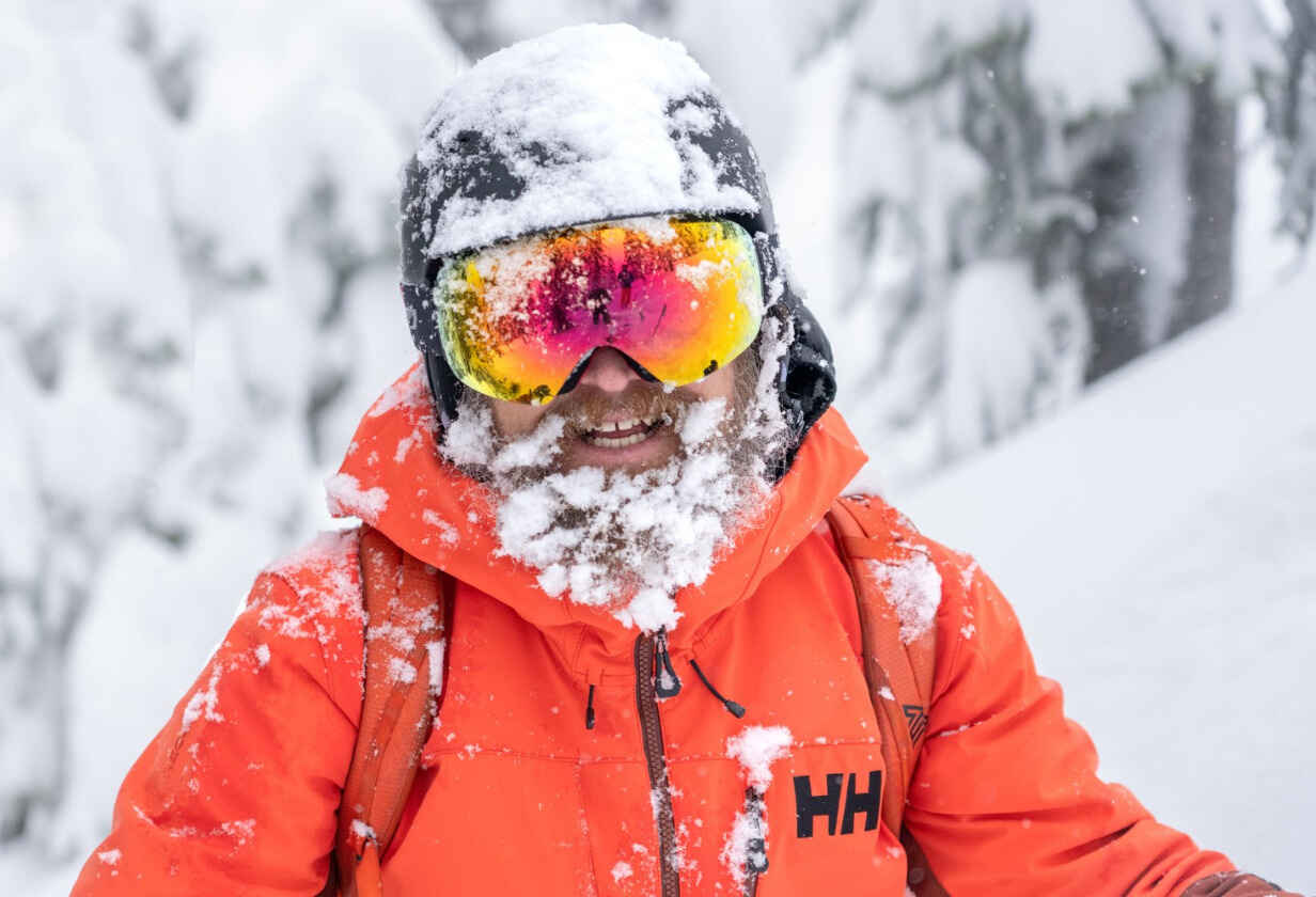 мъж със ски каска и очила в снега с червено яке