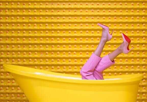 жена с розови обувки с ток и розов панталон в жълта вана