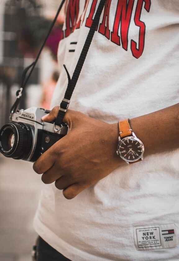 мъж с бяла тениска и часовник държи ретро фотоапарат pentax