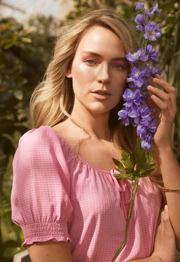 руса жена с розова рокля държи лилаво цвете
